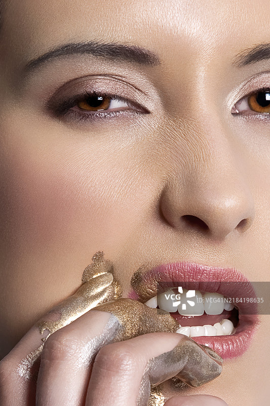 特写肖像，一位女性用手指轻触嘴唇，妆容闪耀金色。图片素材