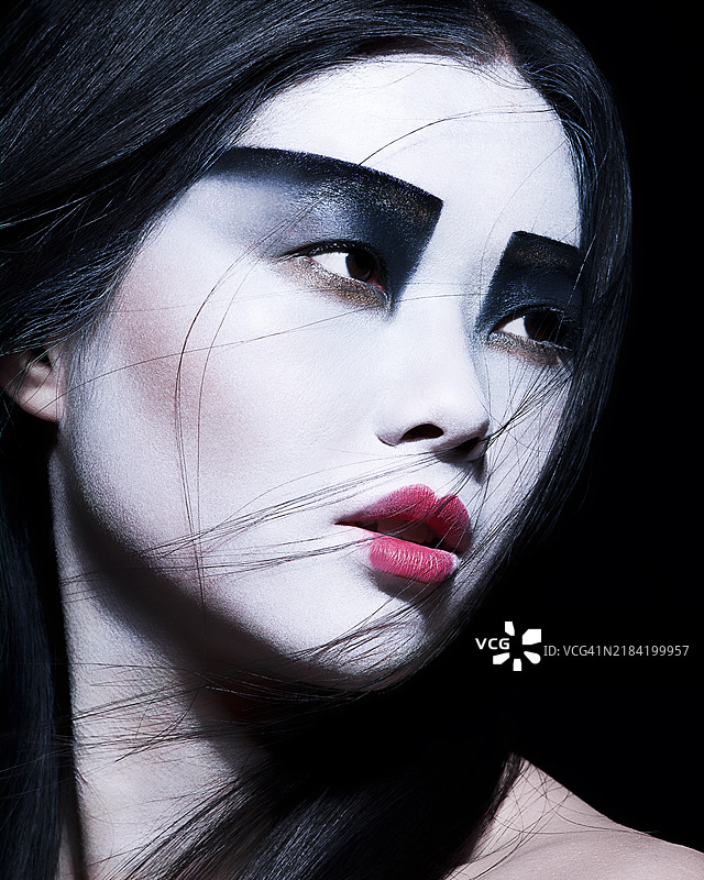 一位女性的戏剧性肖像，脸部化妆采用大胆的黑白色调，鲜艳的红唇，侧目凝视，背景昏暗。图片素材