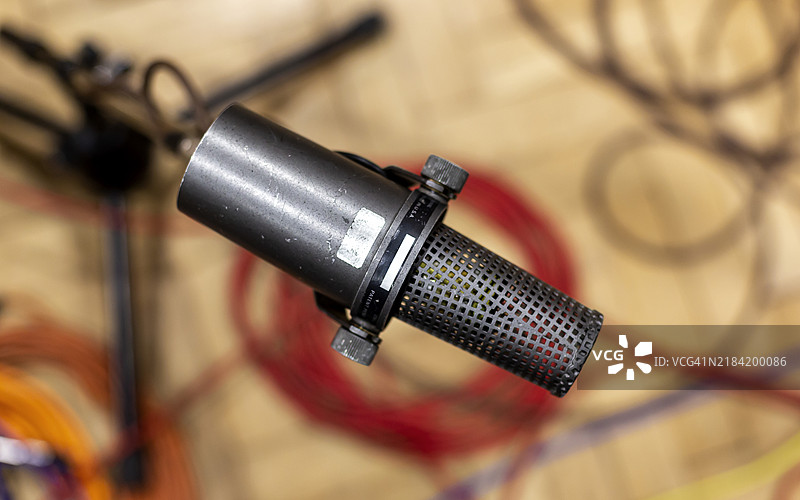 特写镜头下的电容麦克风悬浮在木桌上，背景有电缆。图片素材