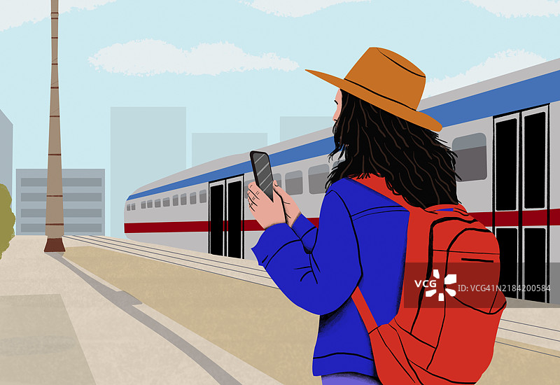 戴着橙色帽子的女人在火车站站着，望着手机，背景有一列火车。图片素材