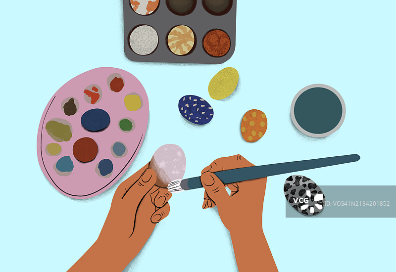 一双手在浅蓝色背景下为彩色鸡蛋上色，旁边有调色板和画笔。图片素材