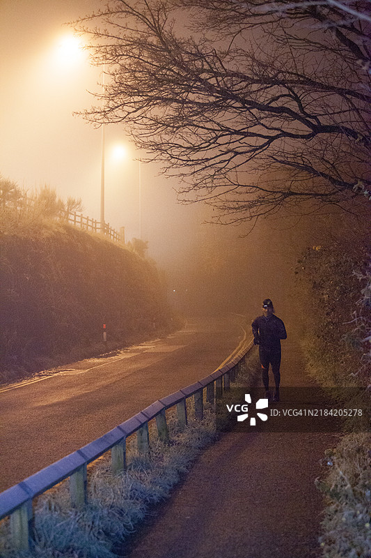 黄昏时分，一个人在雾蒙蒙的路边独自行走，路灯散发着温暖的光芒。图片素材