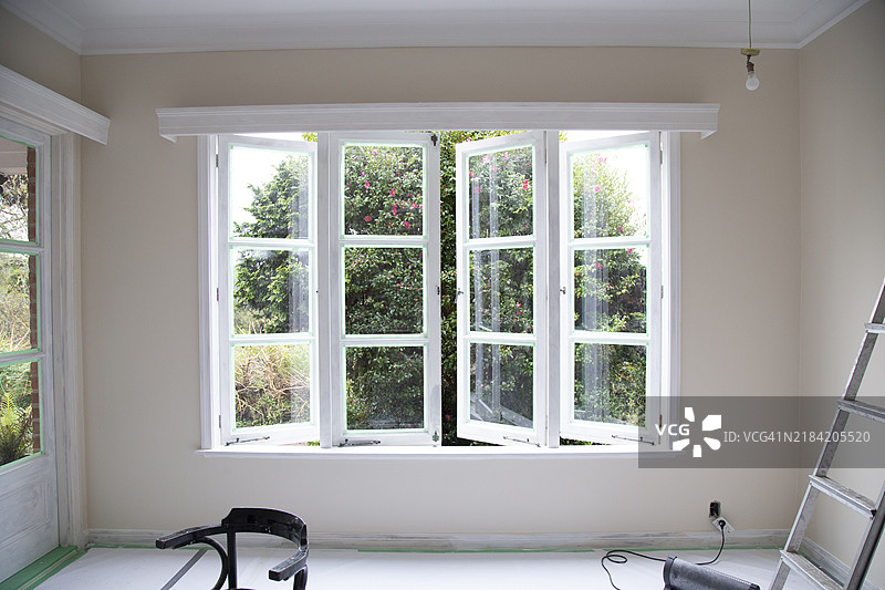 新西兰奥克兰一间刚粉刷的房间内部，窗户敞开，旁边有一把梯子和装修工具。图片素材