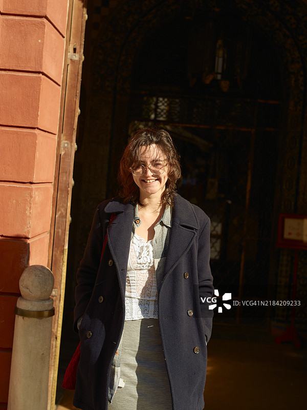 微笑的女性站在阳光下，面前是一扇装饰华丽的建筑入口门。图片素材