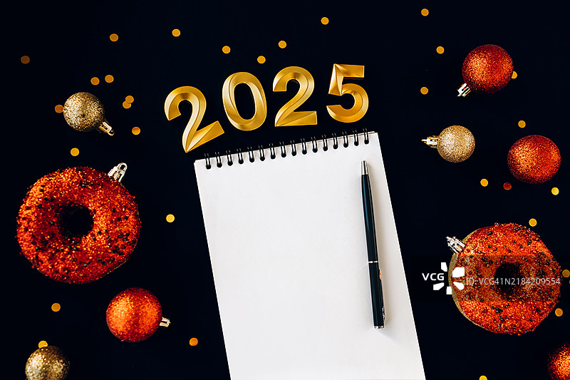 2025年的新年决心和目标。黑色背景上的笔记本、钢笔和节日装饰。目标、决心、计划、行动、清单概念。平铺，留白。图片素材