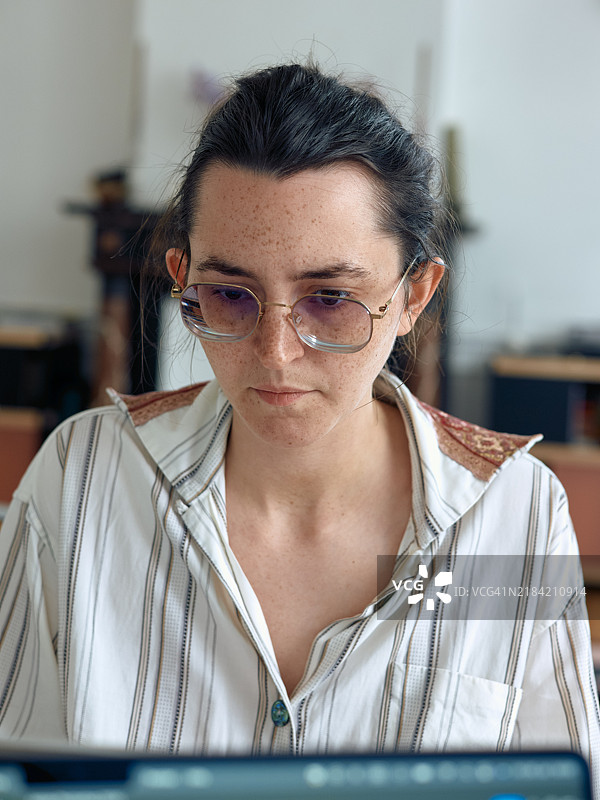 一位专注的戴眼镜的女性在光线充足的房间里使用笔记本电脑。图片素材