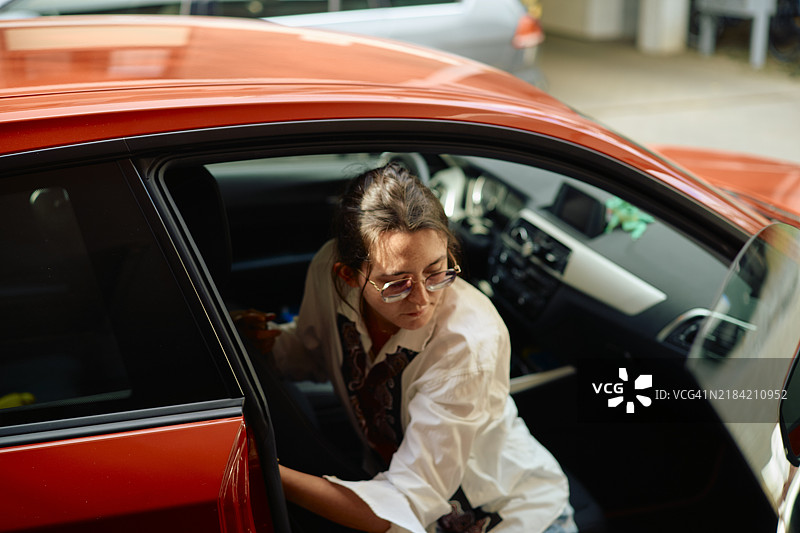 穿着白衬衫的女人正走进一辆车门敞开的红色汽车。图片素材