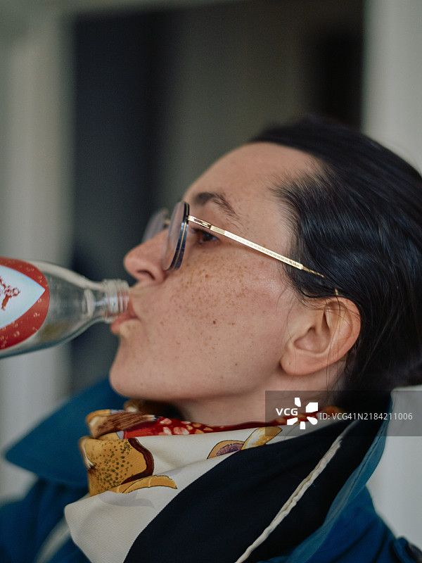 一位戴着眼镜和围巾的女性正在喝汽水瓶里的饮料图片素材