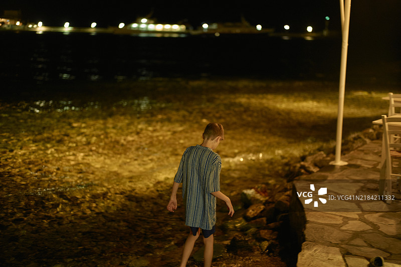 穿着条纹衣服的孩子在夜晚的海边走，周围有柔和的灯光。图片素材