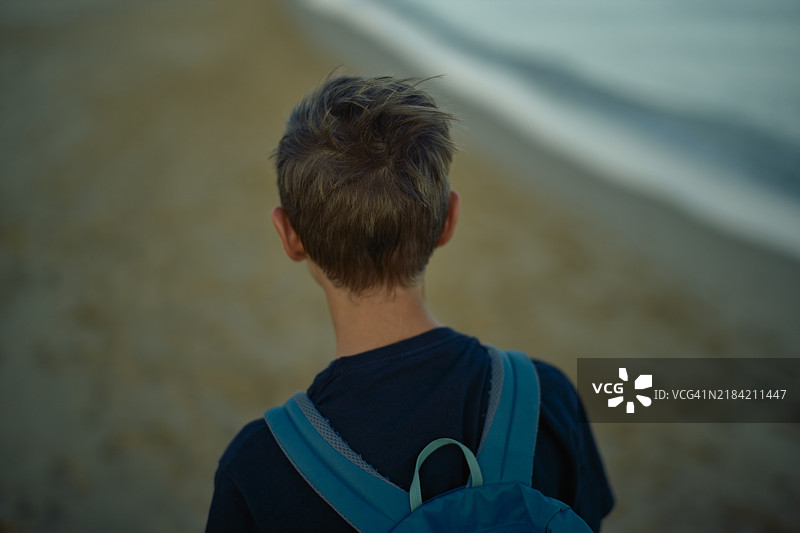 黄昏时分，背着书包的小男孩在沙滩上行走图片素材