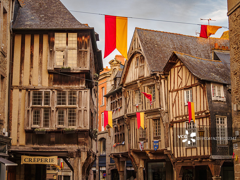 日落时分,迪南中世纪老城梅尔西广场的传统布列塔尼半木结构房屋外立面的特写,木制拱廊、传统旗帜和横梁,科特迪瓦尔省 - 布列塔尼 - 法国西部。图片素材