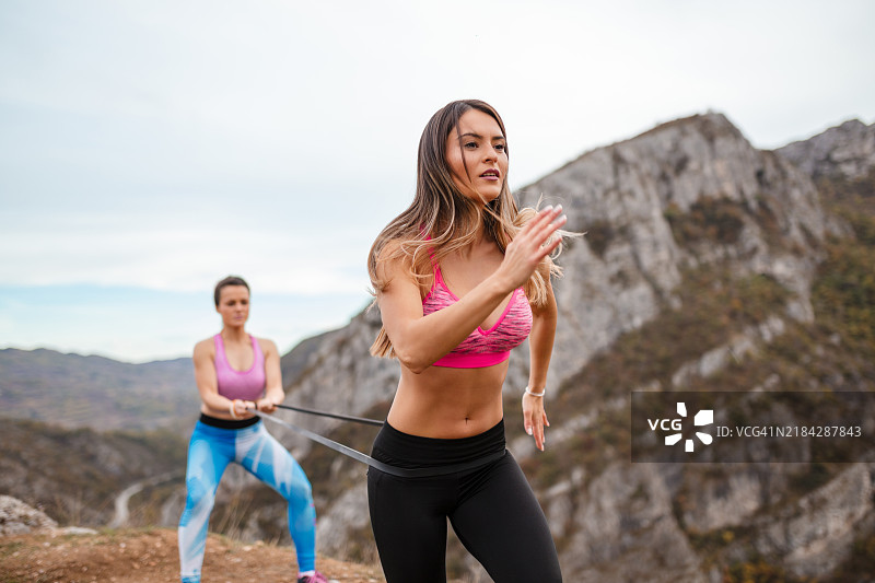 两名女性在风景如画的山地户外使用阻力带慢跑图片素材