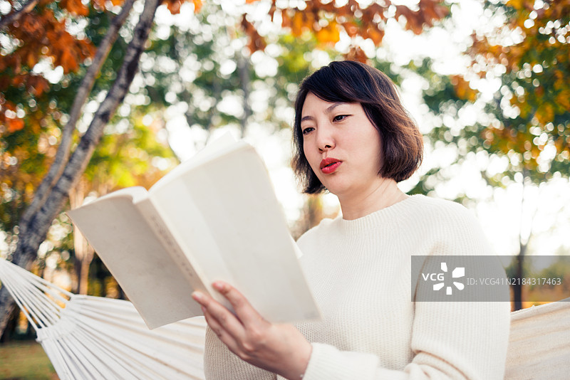 快乐的亚洲女性在吊床上放松地阅读书籍图片素材