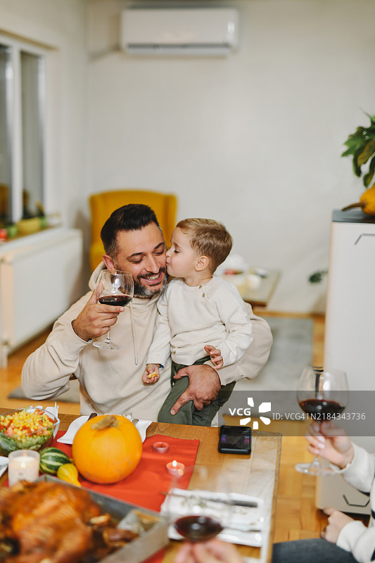 可爱的小男孩在感恩节晚餐庆祝时亲吻父亲的脸颊图片素材