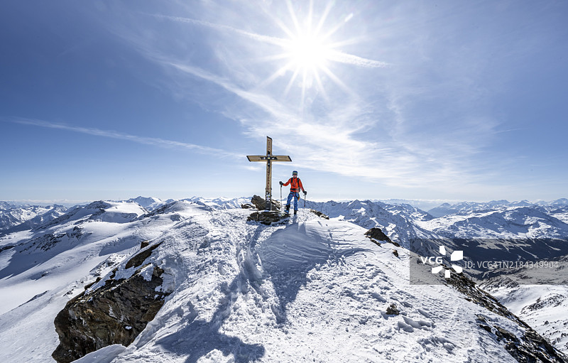 在意大利文斯普豪谷的奥尔特勒阿尔卑斯山，雪覆盖的冬季山景中，登山滑雪者站在切维达莱峰的山顶，山顶十字架、阳光星光和壮丽的山脉全景尽收眼底。图片素材