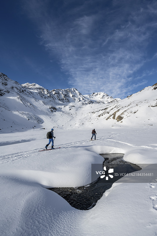 雪覆盖的山地风景中的小溪，滑雪者在山谷中，攀登马德里茨峰，奥尔特勒阿尔卑斯山，芬施高，意大利，欧洲图片素材