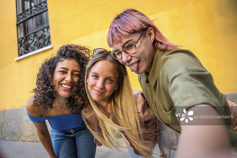 快乐的女性朋友们在街上自拍时做鬼脸并吐舌头图片素材