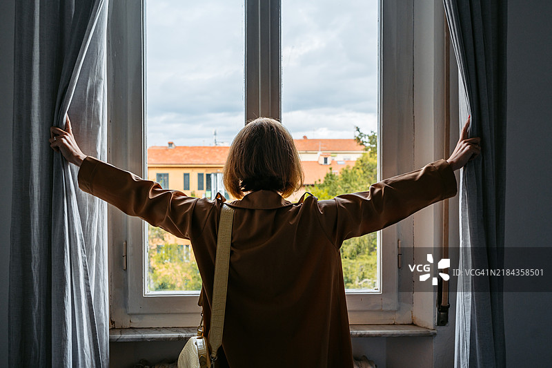 中年女性在意大利比萨的卧室里拉开窗帘图片素材