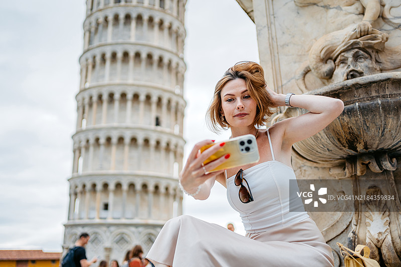 中年女性在比萨斜塔前的天使喷泉旁自拍图片素材