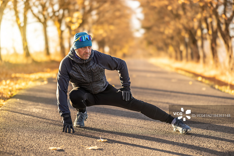 一位健康的成年男性在寒冷的秋晨进行跑步训练前热身。图片素材