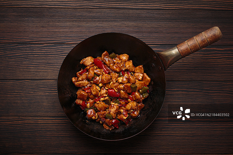 木制桌面上的传统中式菜肴宫保鸡丁在炒锅中。图片素材