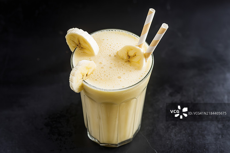 一杯奶油黄色的香蕉奶昔，放置在黑色表面上。图片素材