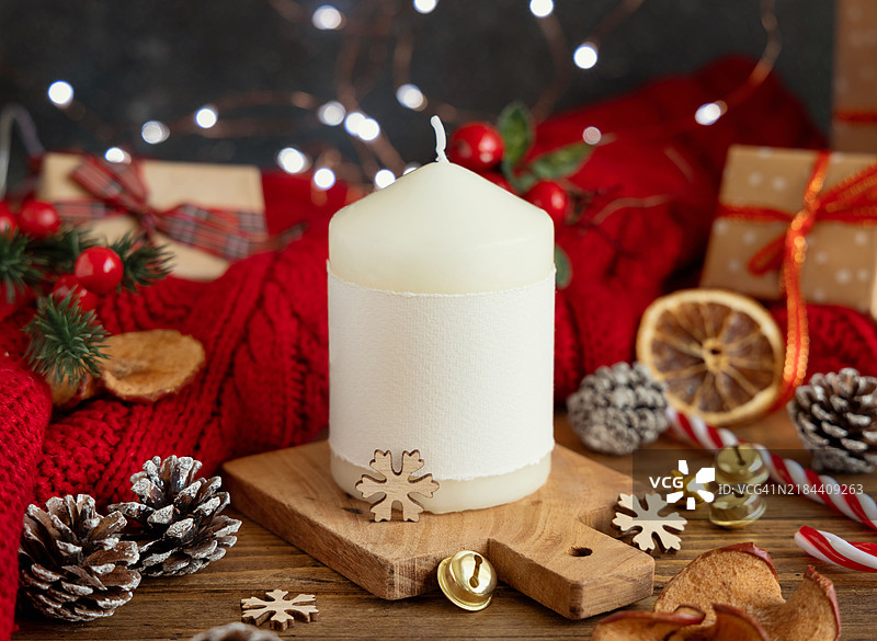 带标签的柱形蜡烛放在红色针织毛衣和圣诞装饰及灯光旁边，冬季样板图片素材