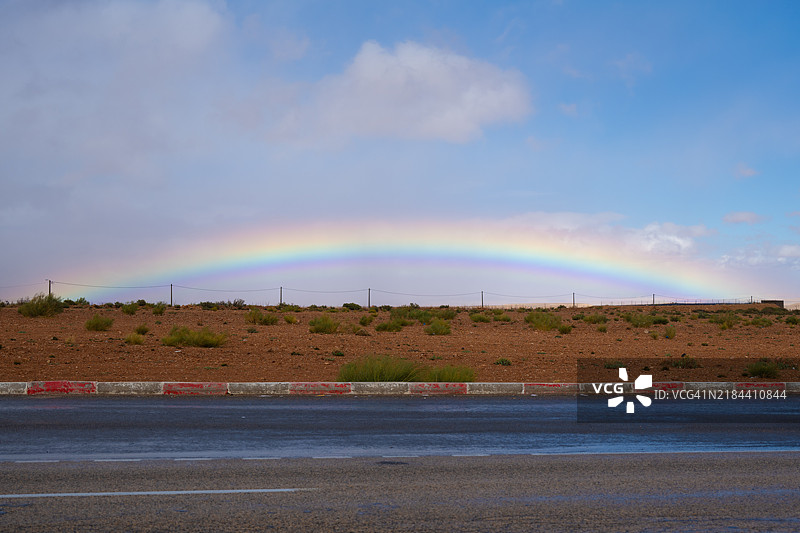 摩洛哥伊夫兰的天空中，彩虹横跨在道路上，景色宜人。图片素材
