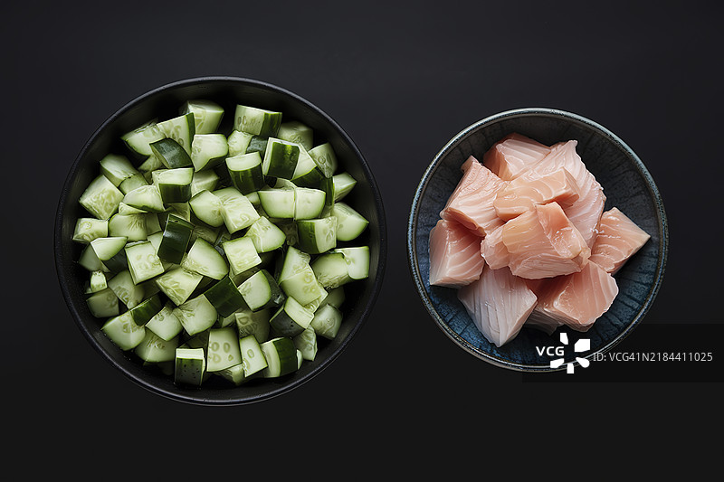 一碗装满切丁的绿色黄瓜，另一碗则装有鱼块。图片素材