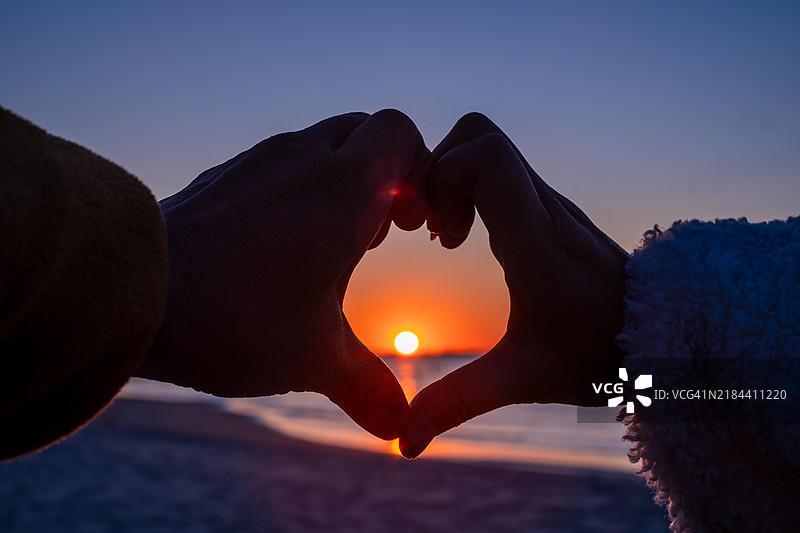 在日落时分，天空背景下的手做成心形。图片素材