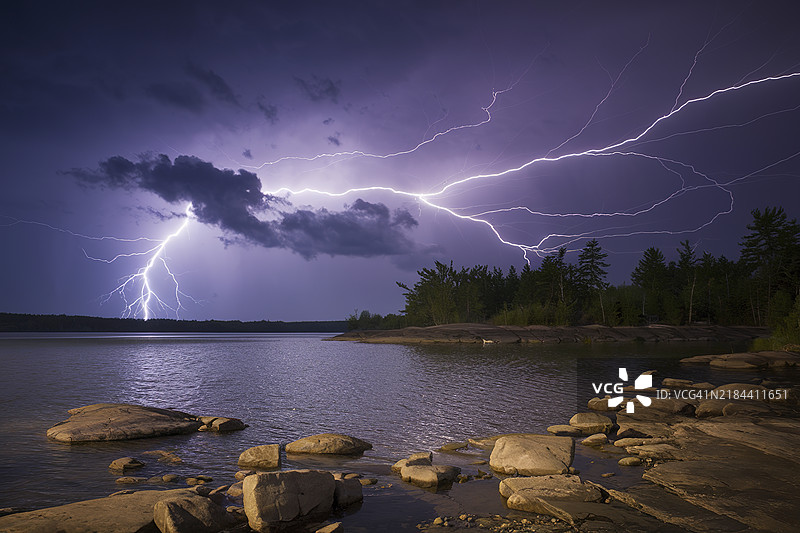 一场戏剧性的雷暴，明亮的闪电划过深紫色的天空，映衬着岩石海岸线和宁静的湖面。图片素材