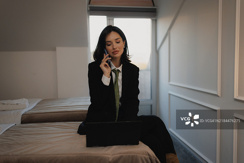 自信时尚的女商人在酒店房间内一边使用笔记本电脑一边接打电话 – 女性理财顾问图片素材