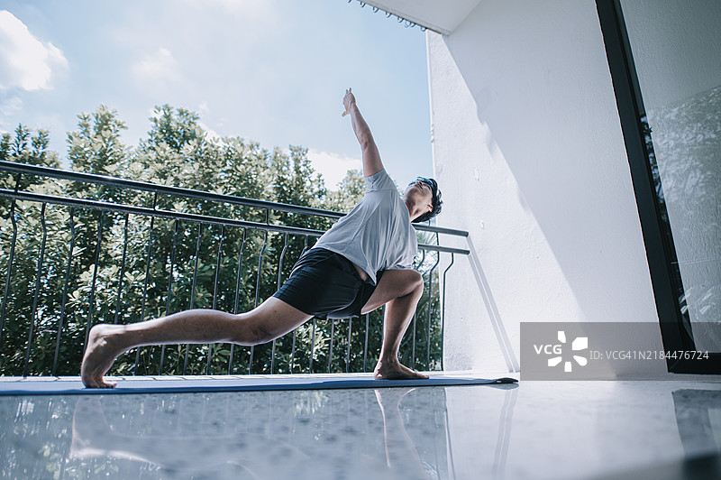 亚洲年轻华裔男性在阳台上练习瑜伽，周末的早晨图片素材