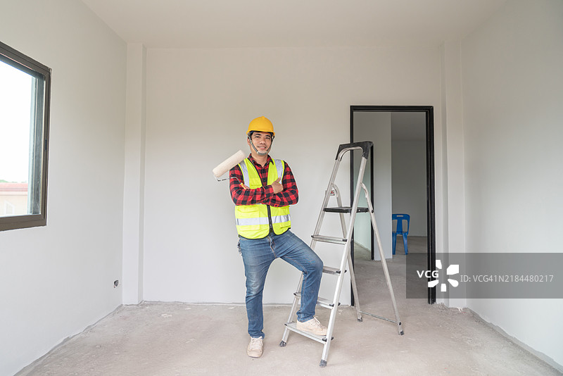 穿着安全装备、手持绘画工具的画家肖像，周围是新家中部分涂鸦的墙壁，温暖而专业。图片素材