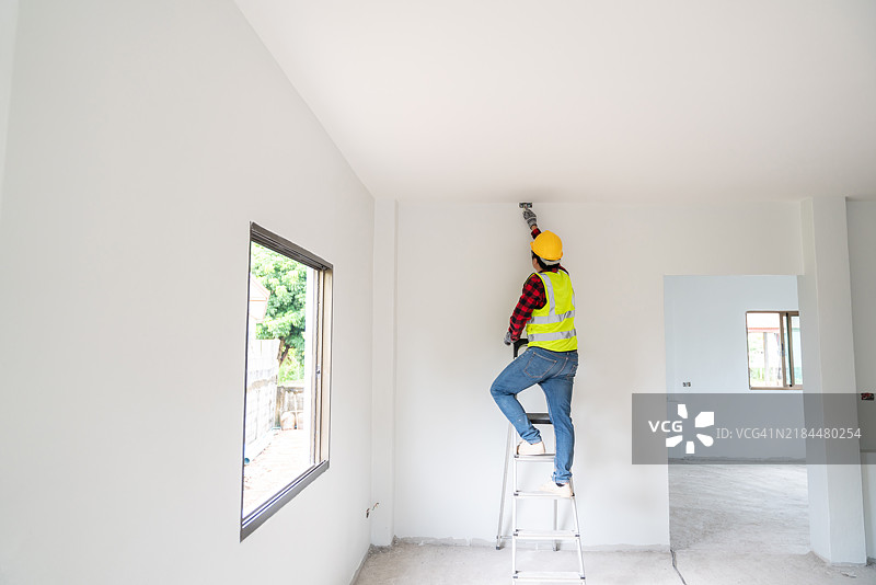 一名电工爬上梯子以接触部分建造房屋的天花板电线，展现出专注和精准，环境干净且专业。图片素材