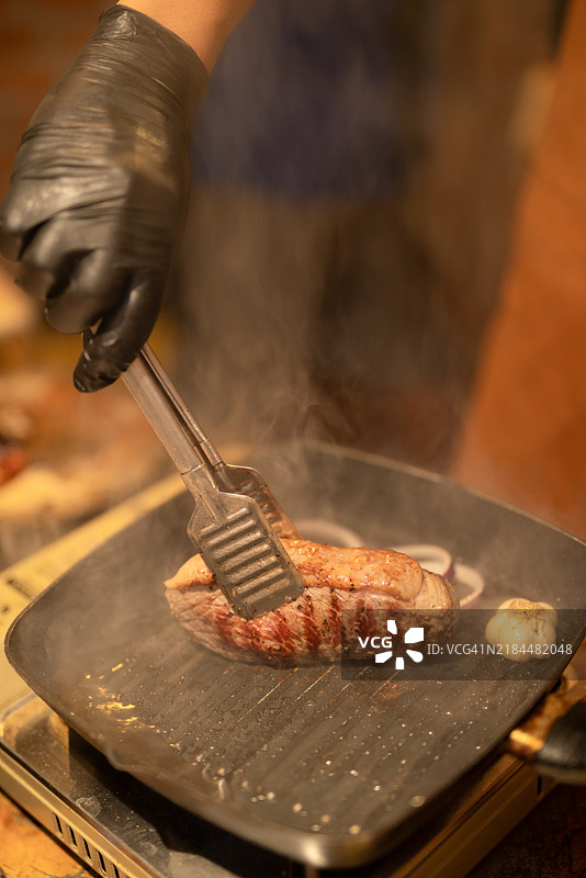 厨师在烤架上翻转一片厚厚的澳大利亚皮卡尼亚肉，完美的烤痕和丰富的油花展现了烹饪技巧。图片素材