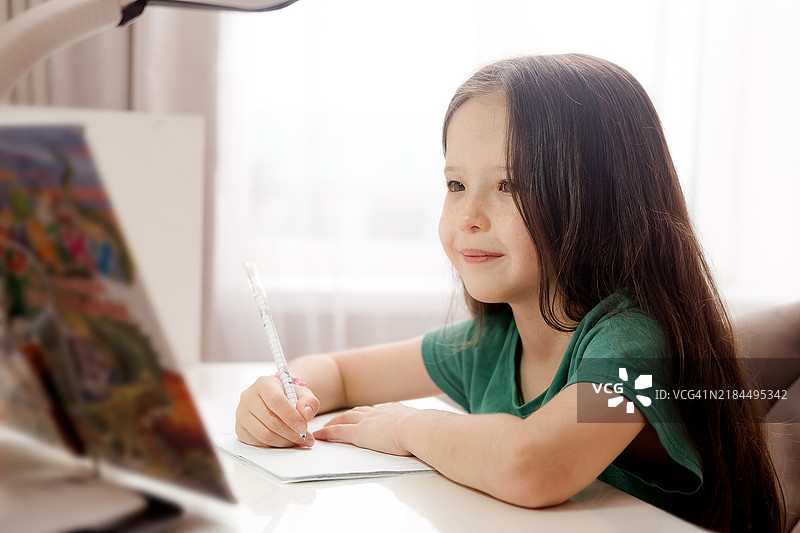 一个小白人女孩坐在桌子旁做作业。图片素材