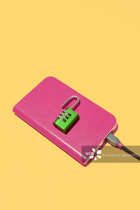 便携式硬盘上方有一个打开的组合锁，象征数据泄露和隐私保护不力。图片素材