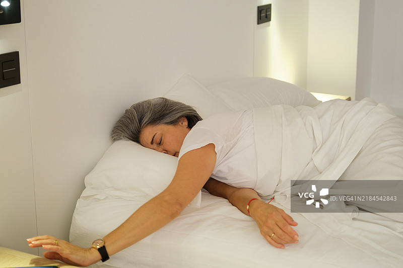 成熟的女性在酒店房间的床上安静地睡觉，伸手去拿闹钟。图片素材