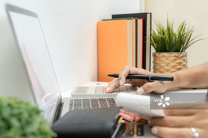 年轻男子使用笔记本电脑查看账单、税务、银行账户余额并计算开支。图片素材