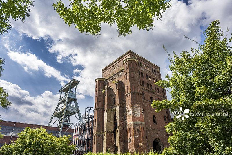 清澈天空下的旧工业建筑和蜿蜒塔，嵌入绿色景观中，赫尔滕的埃瓦尔德矿井蜿蜒塔。图片素材
