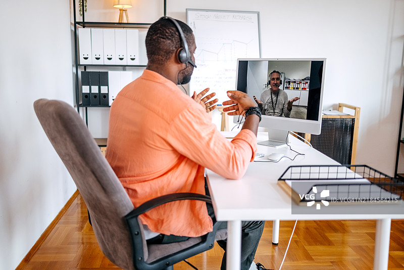 年长和年轻的男性同事一起工作，分享经验，并通过桌面电脑进行视频通话，为年轻同事提供指导。图片素材