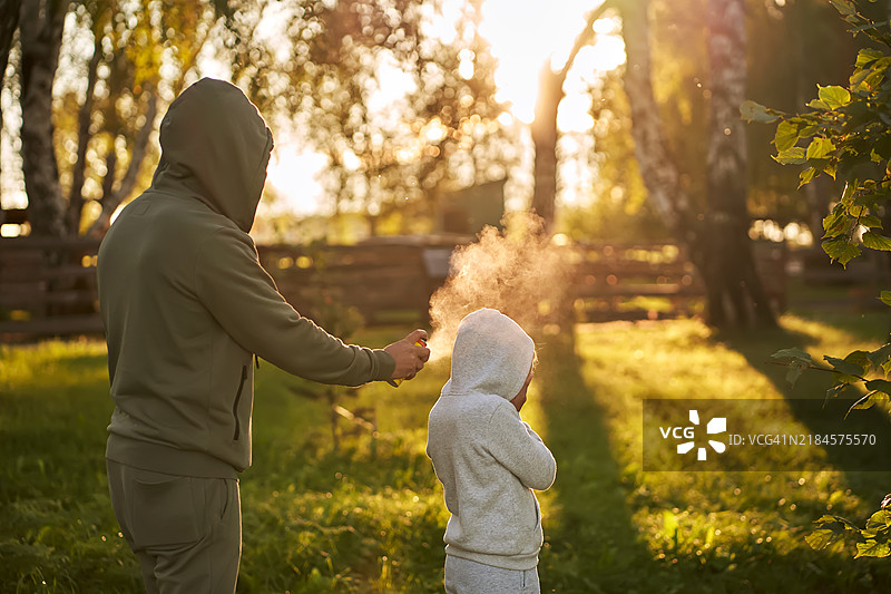 一个男人在森林里给一个孩子喷洒驱虫剂。图片素材