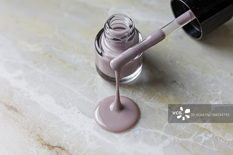 一瓶空白标签的指甲油瓶特写，瓶口滴落一滴指甲油。图片素材
