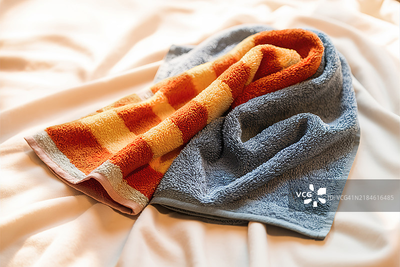 两条毛巾，一条有鲜艳的橙色和黄色条纹图案，另一条是纯蓝色。图片素材