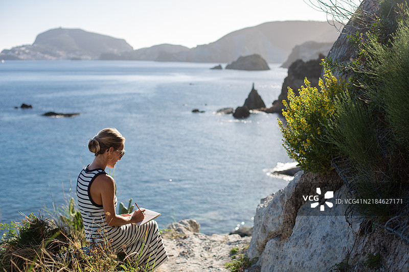 女人坐在海边的岩石上画画图片素材