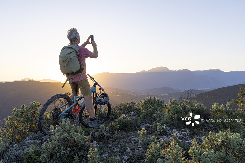 成熟的山地自行车骑士在日出时在山坡上使用手机图片素材