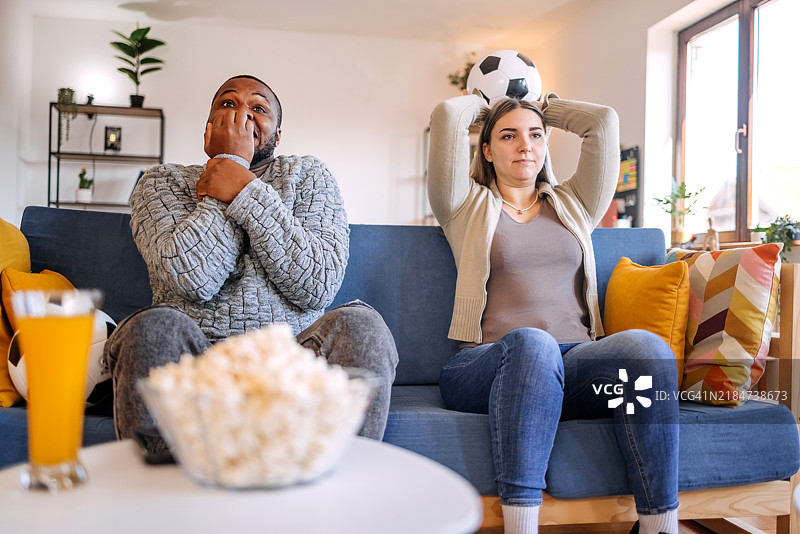 多种族情侣在家中的客厅里一起享受观看足球比赛，期待他们的球队进球。图片素材