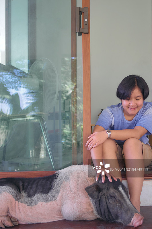 女孩在门廊台阶上轻柔地抚摸她的小猪图片素材