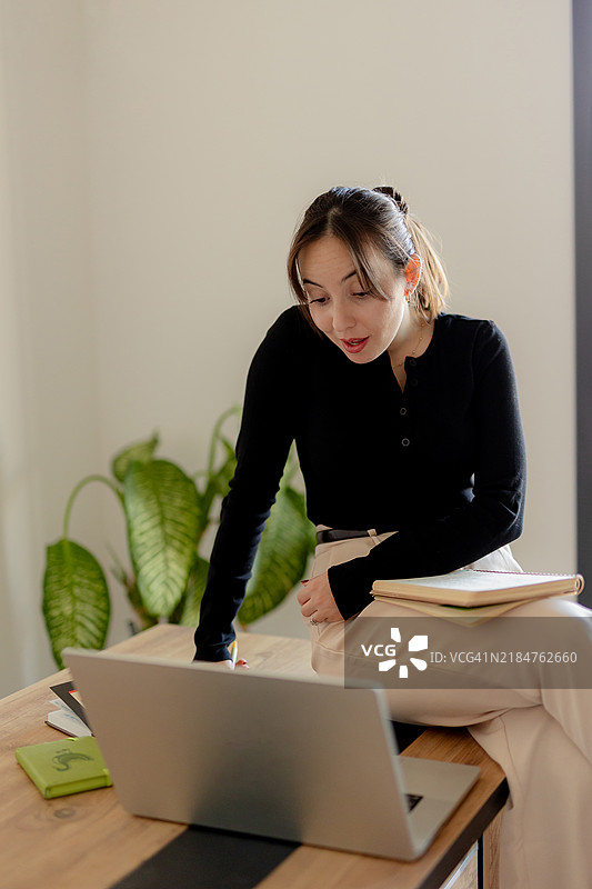 自信的年轻女商人在现代办公室环境中庆祝成功，手边有笔记本电脑和文件。图片素材